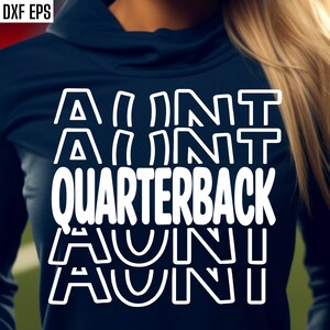 Op de afbeelding: Een wit grafisch ontwerp op een donkerblauw shirt met de tekst "Aunt Quarterback", waarbij het woord "Aunt" vier keer in een gestapelde vorm wordt herhaald.