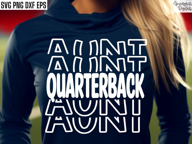 Op de afbeelding: Een wit grafisch ontwerp op een donkerblauw shirt met de tekst "Aunt Quarterback", waarbij het woord "Aunt" vier keer in een gestapelde vorm wordt herhaald.