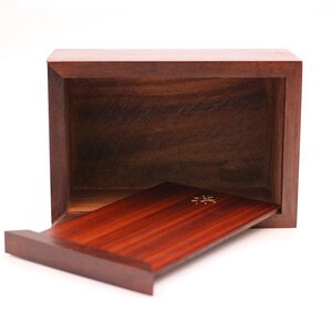 May include: A rectangular wooden box with a sliding tray. The box and tray are made of dark brown wood with a visible wood grain. The tray is partially extended, revealing a gold-colored design.