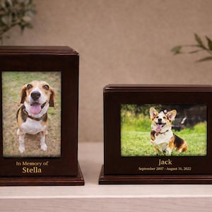 May include: Two dark brown pet urns with framed photos of dogs. The taller urn has a photo of a beagle, with the text "In Memory of Stella". The shorter urn has a photo of a corgi, with the text "Jack September 2007 - August 31, 2022".