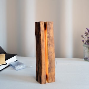 Può includere: Una lampada in legno con un caldo bagliore arancione che emana dal centro. La lampada è realizzata con due pezzi di legno che sono stati uniti, creando un aspetto unico e rustico.