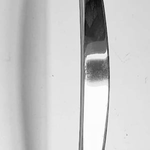 May include: A polished silver door handle with a curved design. The handle has a rectangular base and a rounded top.