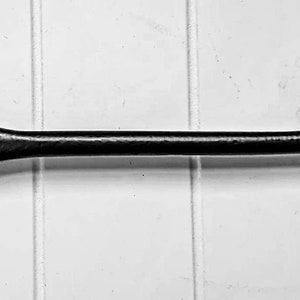 Könnte beinhalten: Schwarzer Türriegel aus Metall mit einem abgerundeten Haken und einer runden Basis. Der Riegel ist an einer weißen Holztür befestigt.