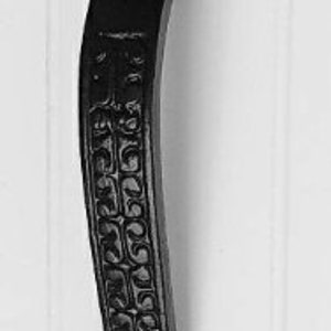 May include: Black, ornate door pull handle with a decorative floral design. The handle is curved with a detailed pattern down the center and a decorative top and bottom. The handle is mounted on a white surface.
