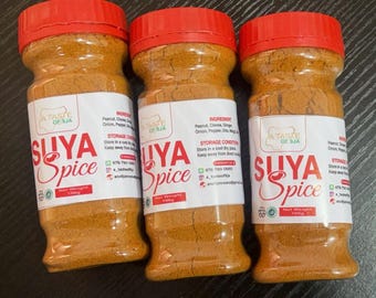 May include: Three bottles of Suya Spice, a blend of peanuts, cloves, ginger, onion, and pepper. Each clear plastic jar has a red lid and a white label with the text "SUYA Spice" in red and the words "A Taste of Sua". The net weight is 100g.
