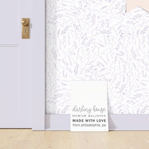 May include: White wallpaper featuring a subtle pattern of lavender-toned leaves and floral designs. A sign in front of the wallpaper reads "darling house PREMIUM WALLPAPER MADE WITH LOVE from philadelphia, pa."