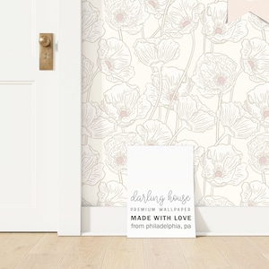 May include: Cream-colored wallpaper with a repeating pattern of large, stylized poppy flowers in light beige and pink. A white sign in front of the wallpaper reads "darling house PREMIUM WALLPAPER MADE WITH LOVE from philadelphia, pa."
