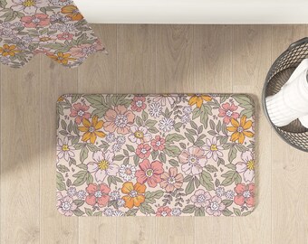 May include: A floral bath mat with a pink, orange, and green pattern. The mat is on a light wood floor.