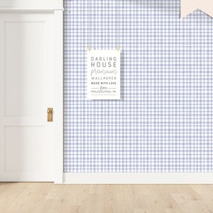 May include: A white door with a gold door handle is next to a wall covered in a light blue and white gingham wallpaper. A white sign with black text hangs on the wall. The sign reads "DARLING HOUSE premium WALLPAPER MADE WITH LOVE from PHILADELPHIA, PA."