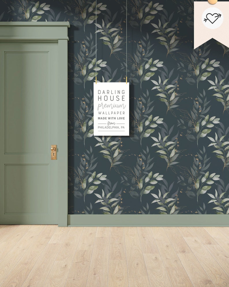 May include: A dark blue wallpaper with a repeating pattern of green leaves and gold accents. The wallpaper is hung in a room with a green door and light wood floors. A sign hanging on the wall reads "Darling House Premium Wallpaper Made with Love from Philadelphia, PA."