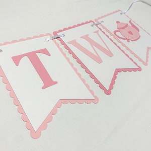 May include: Pink and white banner with the word "TWO" and a pink teapot illustration. The banner is made of cardstock and has a scalloped edge.