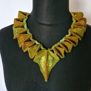 Könnte beinhalten: Eine grüne und braune Filzkette mit einem spitzen, dreieckigen Anhänger. Die Kette besteht aus mehreren Schichten Filz, die einen gerüschten Effekt erzeugen. Der Anhänger ist mit kleinen grünen Perlen verziert.