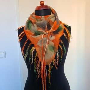 Könnte beinhalten: Ein dreieckiger Schal mit einem farbenfrohen abstrakten Muster in Orange-, Grün- und Brauntönen. Der Schal hat lange Fransen an den Rändern und ist aus gefilzter Wolle gefertigt.