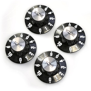 Puede incluir: Cuatro botones de guitarra negros con números y letras blancas. Dos botones dicen "VOLUME" y dos botones dicen "TONE".