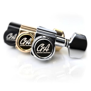 May include: Close-up of three guitar tuning machines in black, gold, and silver. Each machine has a circular black face with the white text "CA GUITAR ANATOMY". The tuning pegs are visible, and the background is white.