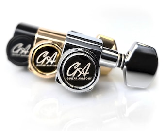 May include: Close-up of three guitar tuning machines in black, gold, and silver. Each machine has a circular black face with the white text "CA GUITAR ANATOMY". The tuning pegs are visible, and the background is white.