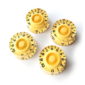 Pode incluir: Quatro botões de guitarra creme com marcações numéricas pretas de 0 a 10. Cada botão tem uma seção central elevada e um mostrador circular numerado. Os botões estão dispostos sobre um fundo branco.