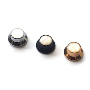 Puede incluir: Tres botones de guitarra con una parte superior de nácar blanco y bases metálicas de diferentes colores: plata, negro y oro.