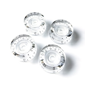 Puede incluir: Cuatro pomos de plástico transparente con números y marcas negras. Los pomos están numerados del 0 al 10.