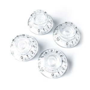 Puede incluir: Cuatro pomos de plástico transparente con números y marcas negras. Los pomos están numerados del 0 al 10.