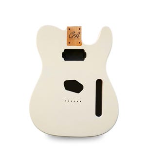 Könnte beinhalten: Ein unfertiger cremeweißer E-Gitarrenkorpus mit Single-Cutaway-Design. Die Halstasche aus Holz zeigt den schwarzen Logo-Schriftzug GA GUITAR ANATOMY. Der Korpus enthält gefräste Aussparungen für Tonabnehmer und Brücke sowie sechs Saitendurchführungen.