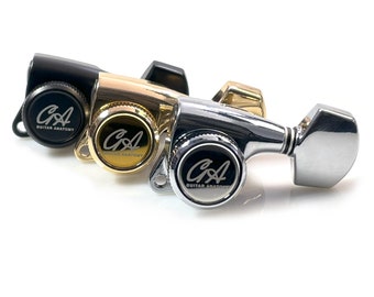 May include: Three guitar tuning machines in black, gold, and silver. Each machine has a circular knob with the text "CA GUITAR ANATOMY" in a circular design. The tuning machines are set against a white background.