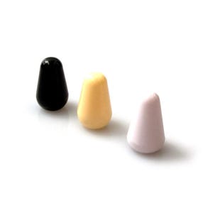 Könnte beinhalten: Drei Gitarrenschalterspitzen in einer Reihe. Die Spitzen sind tropfenförmig und in drei Farben: Schwarz, Creme und Hellrosa. Die Spitzen bestehen aus glänzendem Material und sind vor weißem Hintergrund angeordnet.