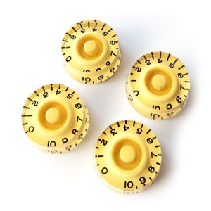 Puede incluir: Cuatro botones de guitarra amarillos con números negros y un botón central negro. Los números en los botones van del 1 al 10.