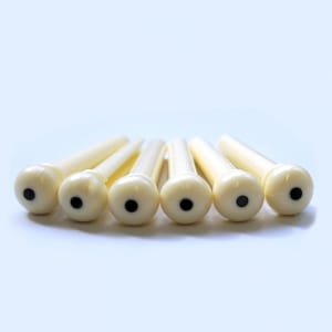 May include: Six white guitar tuning pegs with black dots in the center.