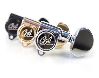 May include: Three guitar tuning machines in black, gold, and silver. Each machine has a circular face with the text "GA Guitar Anatomy" in a white font. The tuning pegs are in a row, with the silver one in the foreground.