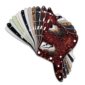 May include: A collection of 14 guitar pickguards in various colors and patterns, including black, white, tortoise shell, and pearloid. The pickguards are arranged in a fan shape, with the tortoise shell pickguard at the bottom.