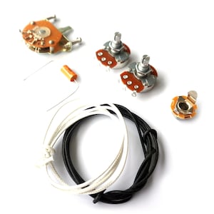 Könnte beinhalten: Eine Sammlung von Gitarrenteilen, darunter ein Schalter, Potentiometer, ein Kondensator, eine Buchse und schwarze und weiße Drähte, auf weißem Hintergrund. Die Komponenten sind neu.