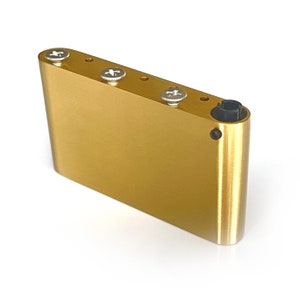 May include: Gold-colored metal guitar bridge with four screw holes and a black output jack.