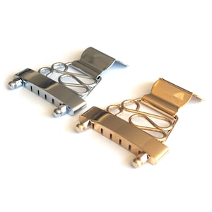 May include: Two guitar bridge saddles, one in gold and one in silver. Both feature a decorative design and six slots for strings.