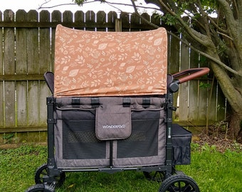 May include: A black and gray wagon with a brown and white patterned canopy. The wagon has a black mesh storage area and the words "Wonderfold" printed on the side. The wagon is sitting on a green grassy lawn.