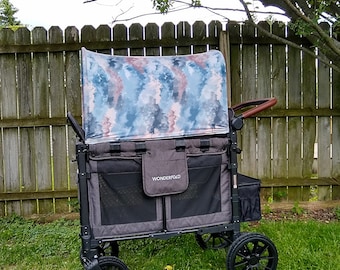 May include: A gray and black wagon with a blue and pink patterned canopy. The wagon has a black handle and four black wheels. The wagon is labeled "Wonderfold" and is sitting on green grass.