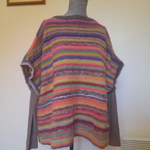 Peut inclure: Un poncho rayé coloré avec un col rond et des manches courtes. Le poncho présente des rayures horizontales de différentes couleurs, notamment rose, orange, vert, violet et gris. Le vêtement est présenté sur un mannequin.