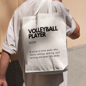 May include: White tote bag with black text that reads "VOLLEYBALL PLAYER NOUN A ninja in knee pads, who thinks setting, spiking, and serving are basic life skills."