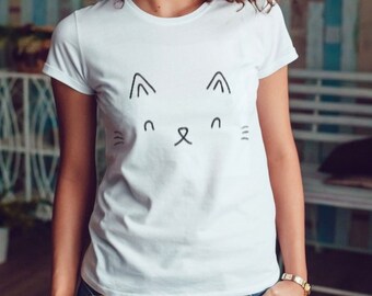 Könnte beinhalten: Weißes T-Shirt mit einem minimalistischen Katzen-Gesicht-Design. Die Grafik verwendet einfache schwarze Linien, um die Ohren, Augen, Nase und Schnurrhaare der Katze zu bilden. Das T-Shirt hat einen klassischen Rundhalsausschnitt.