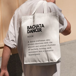 May include: White tote bag with black text that reads "BACHATA DANCER NOUN A dance craftsman who sculpts emotions with the smooth and sensual rhythms of bachata, turning each movement into a romantic masterpiece."