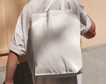 Può includere: Una persona indossa una maglietta bianca e jeans blu e porta una borsa tote bianca sulla spalla.