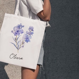 May include: A white tote bag with a watercolor design of purple flowers and the name "Olivia" printed on the front.