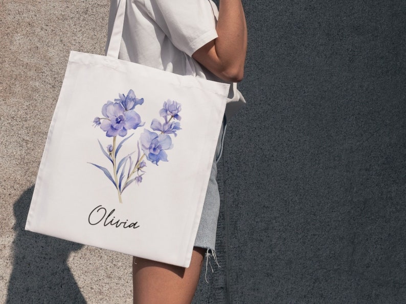 May include: A white tote bag with a watercolor design of purple flowers and the name "Olivia" printed on the front.