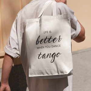 May include: White tote bag with black text that reads "Life is better when you dance tango".