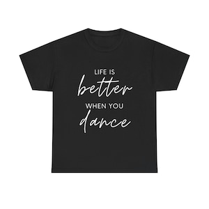 May include: Black t-shirt featuring the white text "LIFE IS better WHEN YOU dance". The crew neck shirt has a handwritten style font. The material appears to be soft. The t-shirt is a classic style.