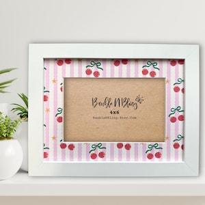 May include: A white 4x6 inch picture frame with a pink and white striped border adorned with cherry illustrations. The frame features the text "Bauble N Bling" and the Etsy shop URL.