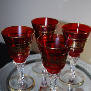May include: Four red glass stemmed goblets with gold trim on a mirrored tray. The goblets have a rounded bowl and a delicate stem.