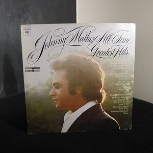 May include: A vinyl record album cover featuring a portrait of Johnny Mathis, a singer, with the title "Johnny Mathis All-Time Greatest Hits" and a list of songs on the album.