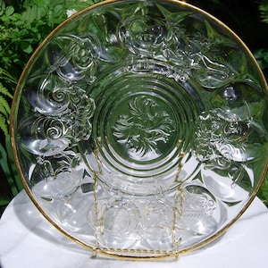 Peut inclure: Un plat de service en verre transparent avec un bord doré et des motifs gravés complexes. Le plat est sur un support blanc.