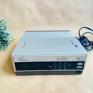 May include: A silver and black Panasonic Programmable Tuner/Timer with a digital display and buttons for channel selection, timer, and VCR functions.